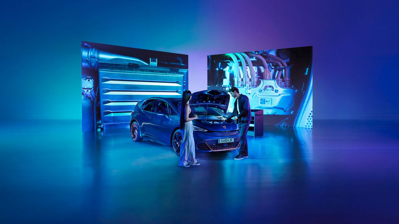 Eine Frau und ein Mann blicken bei geöffneter Kühlerhaube auf den Motor eines CUPRA Born