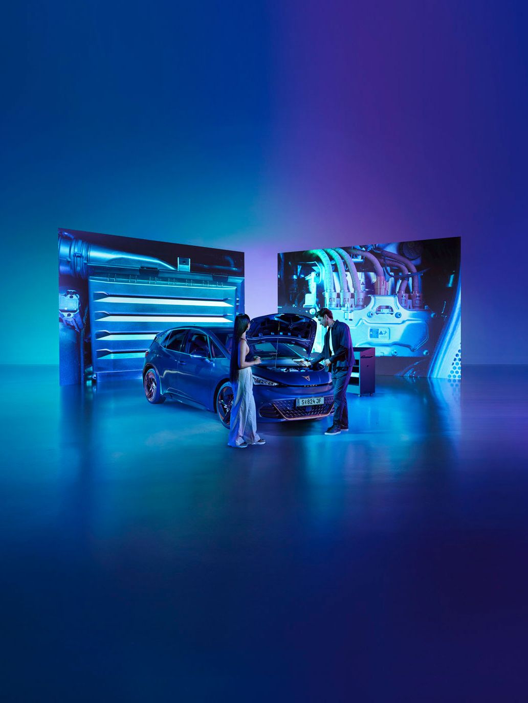 Eine Frau und ein Mann blicken bei geöffneter Kühlerhaube auf den Motor eines CUPRA Born