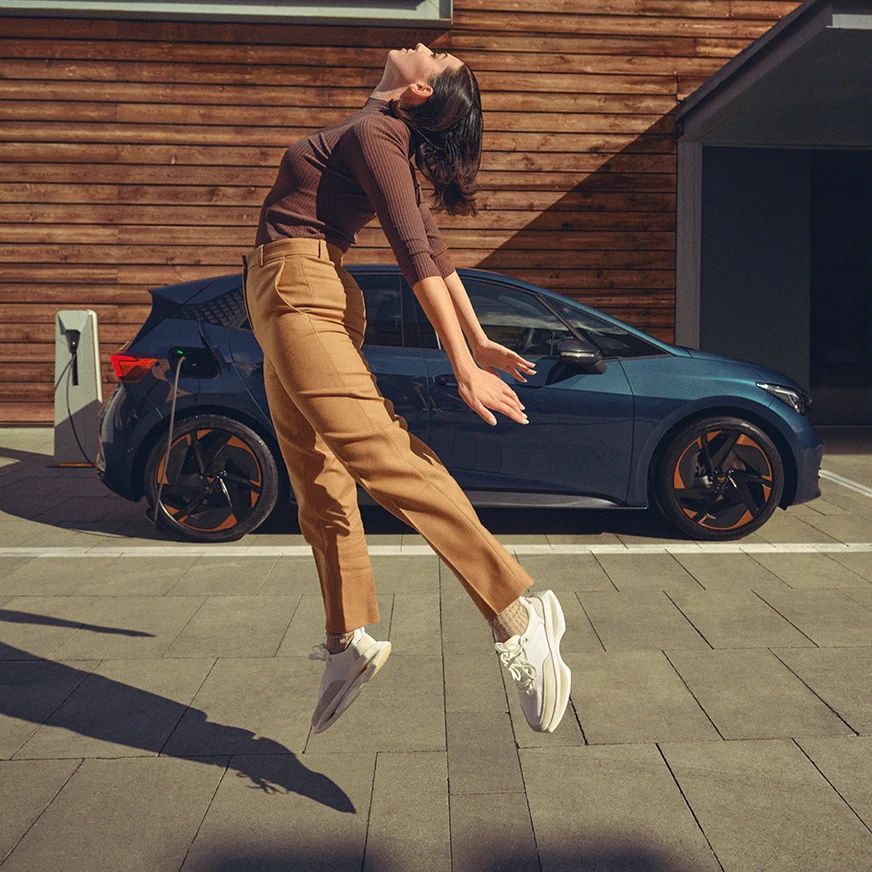 Eine Frau springt in die Luft, im HIntergrund ein CUPRA Born