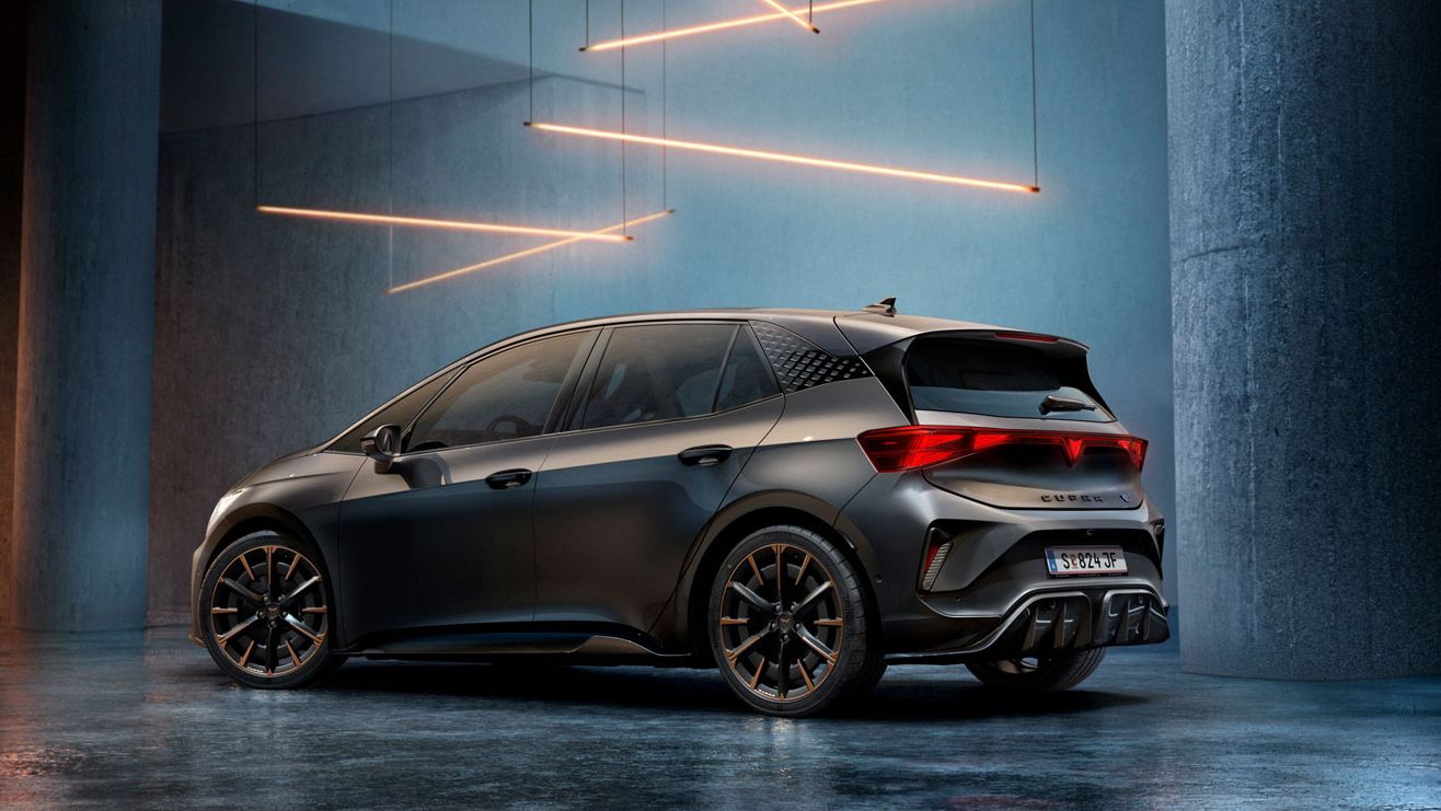 Ein CUPRA Born steht in einem stilvoll beleuchteten, industriellen Raum mit Betonwänden und -säulen. Von der Decke hängen mehrere lineare Lichtquellen, die ein elegantes Ambiente schaffen. Das Fahrzeug ist rückseitig zu sehen und reflektiert das Licht auf dem glänzenden Boden.